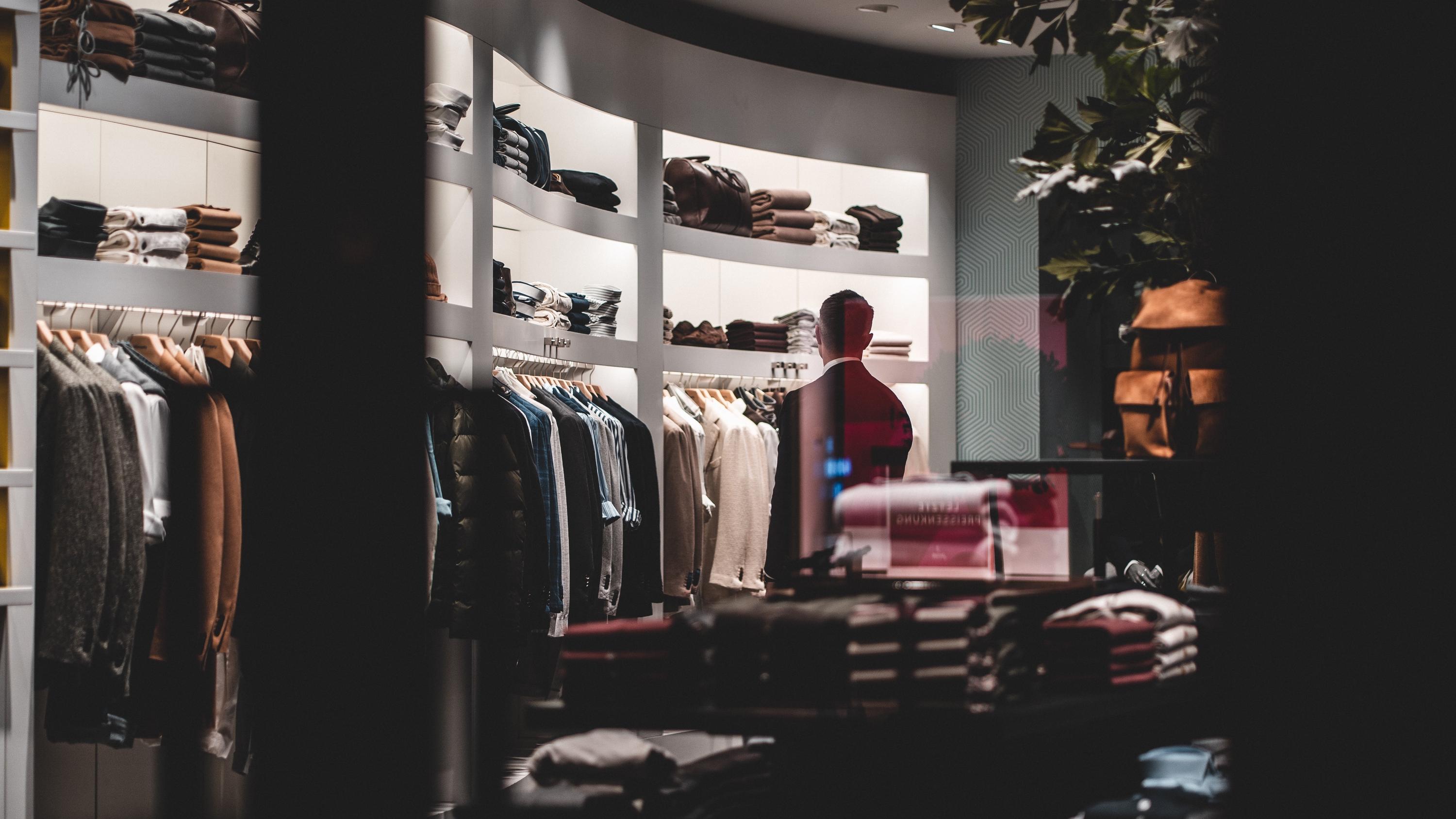 Man looking at folded clothing items on a shelf in clothing store