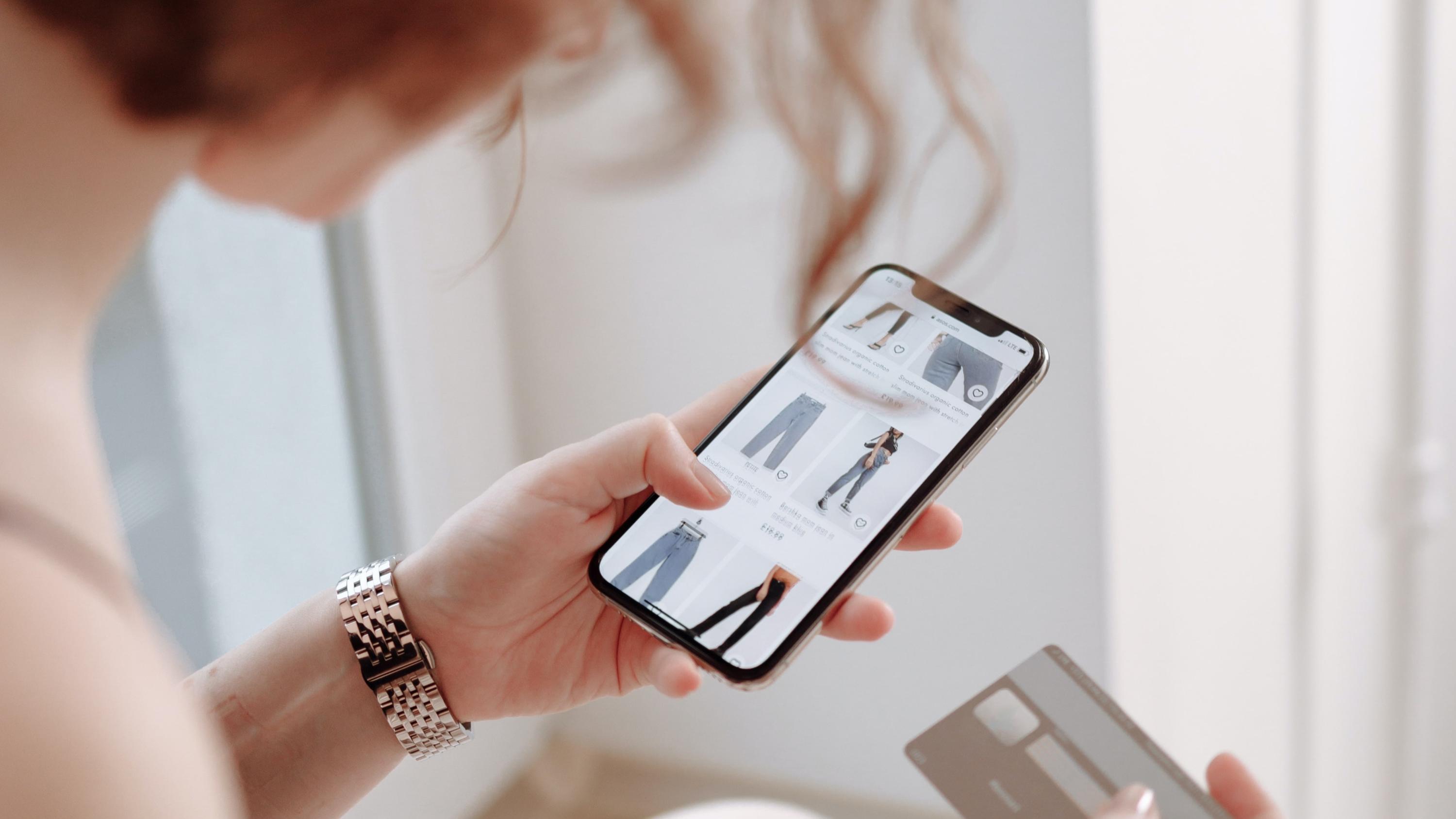 Woman shopping for pants on her smartphone with credit card in other hand