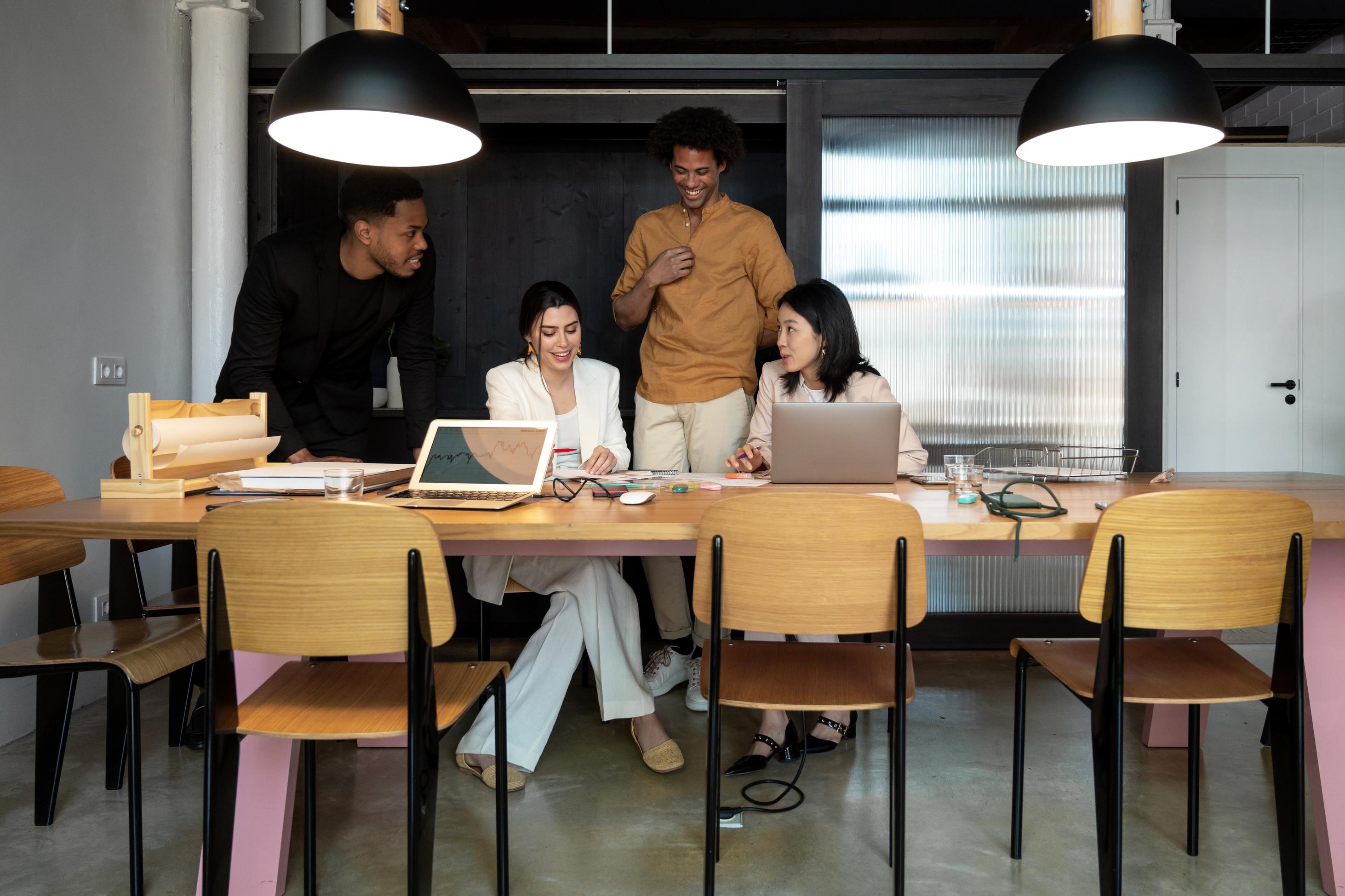 Four people at a conference table talking with laptops and notebooks